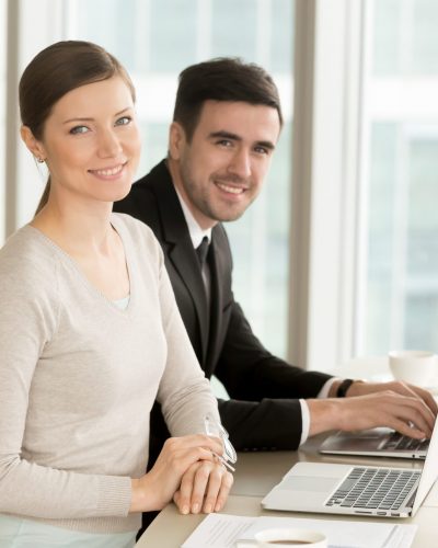 Smiling professional businesswoman and businessman looking at camera, leaders posing with laptops at desk, executive team portrait, internet marketing, corporate education, online business concept